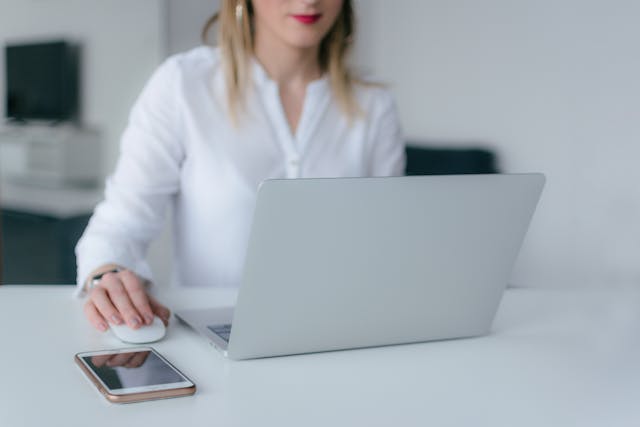 Person in a white shirt working on their computer with a phone next to them